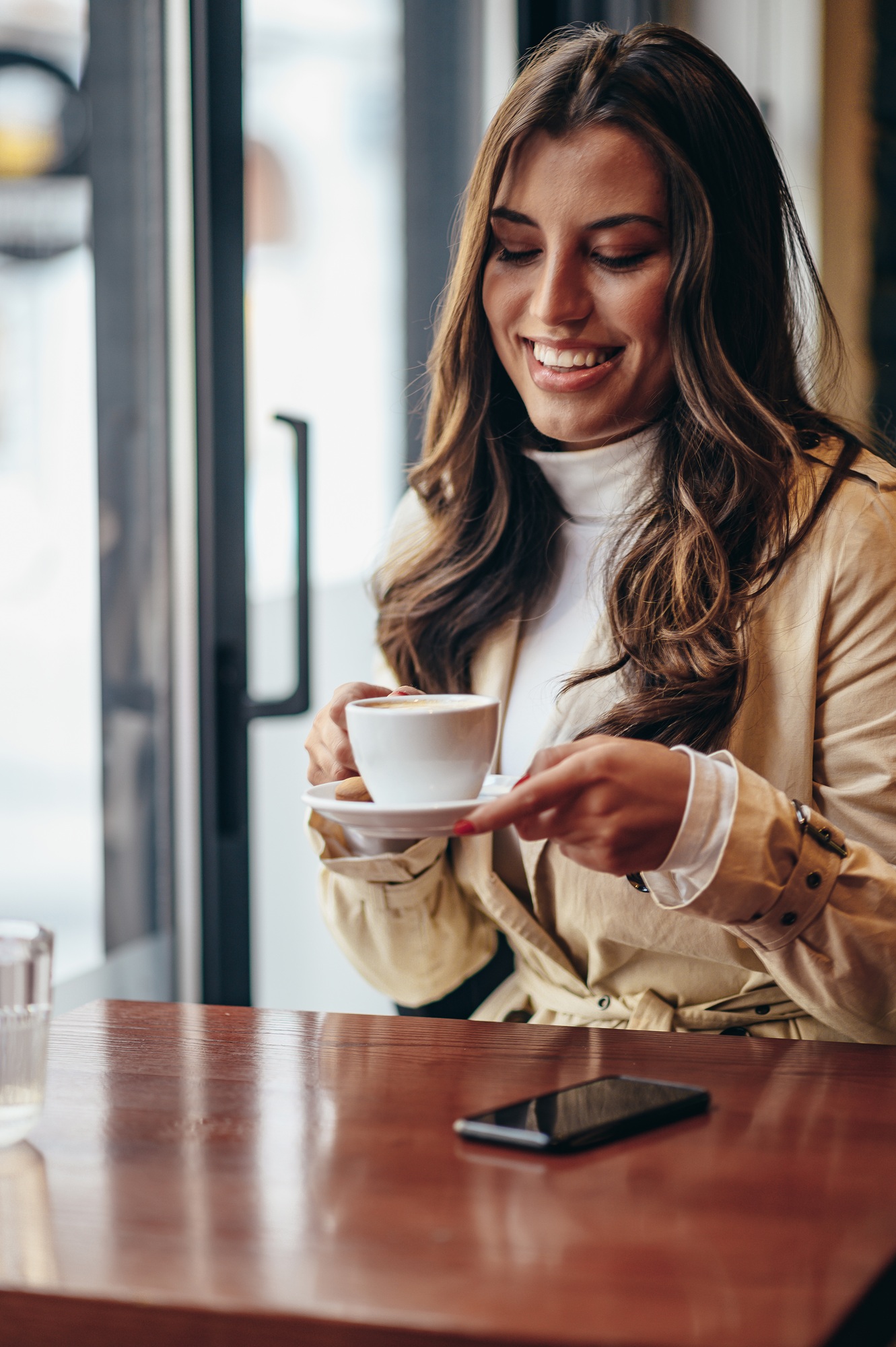 Woman using a smartphone and drinking coffee while sitting in a coffee shop